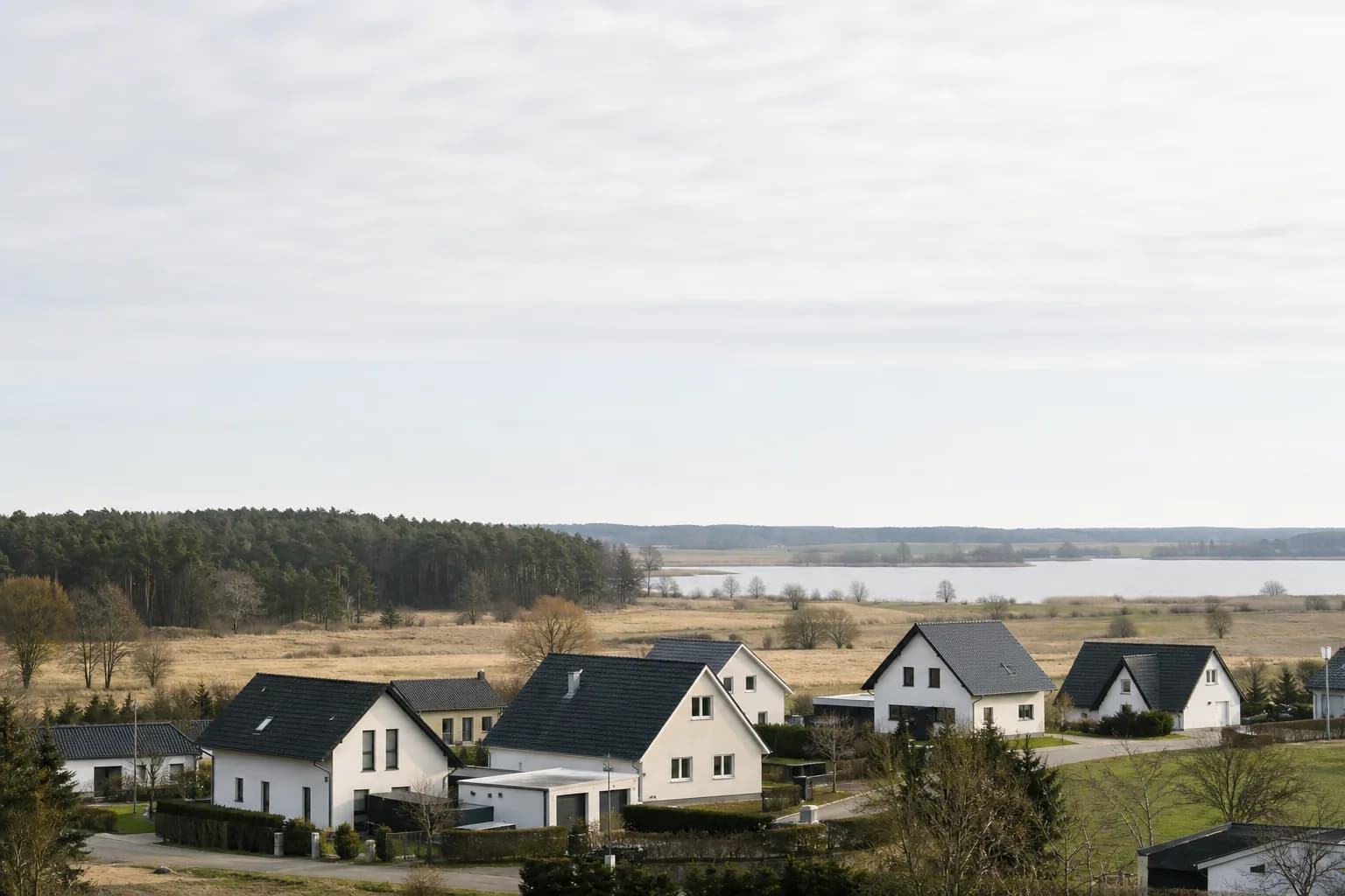 Wohnhäuser in weiter Brandenburger Landschaft mit Kiefernwald und See