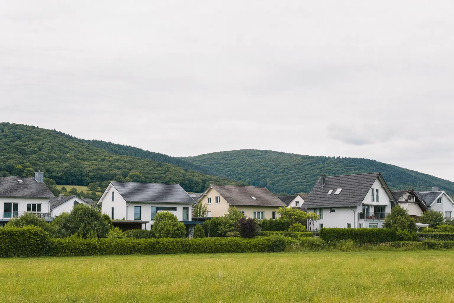 Wohnhäuser vor bewaldeten Mittelgebirgshügeln in Hessen